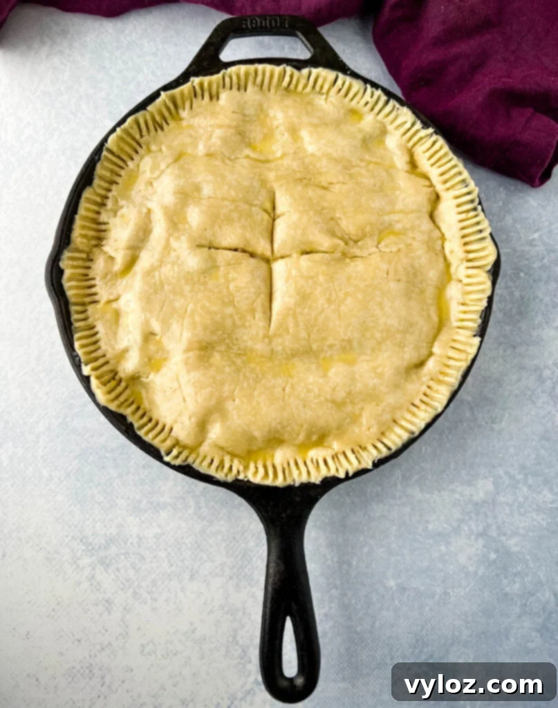 An unbaked seafood pot pie in a cast iron skillet before baking, showing the top crust and vents.
