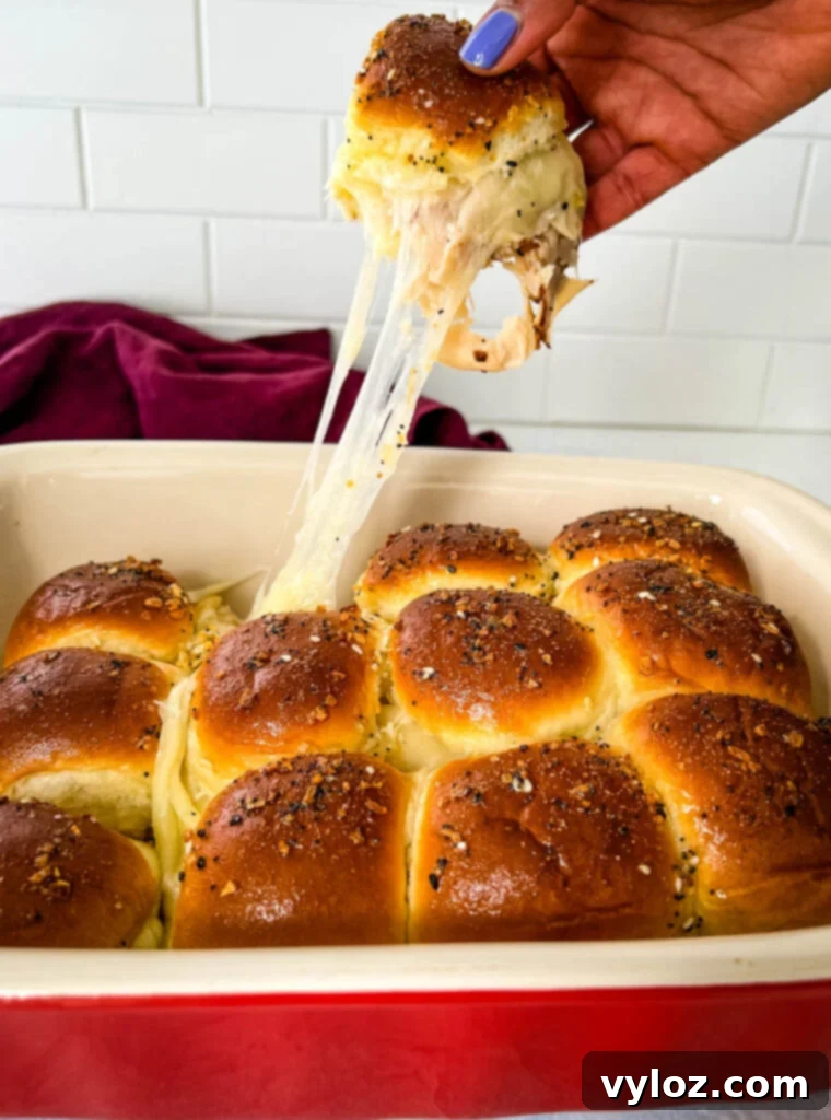 Cheesy Turkey Sliders 2 golden brown turkey and cheese slider with melted cheese being held by a person