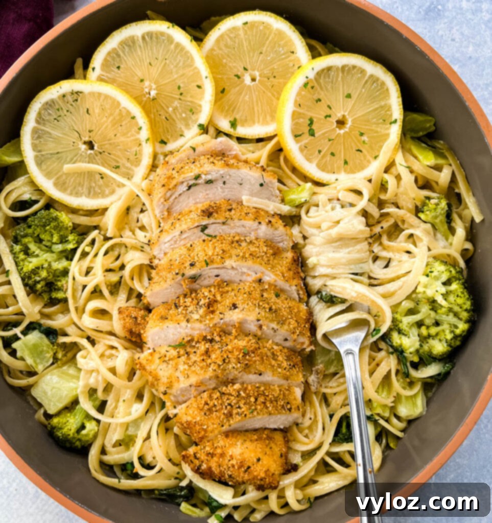 Creamy lemon chicken pasta in a pan with fresh lemons, spinach, and broccoli, ready to serve.