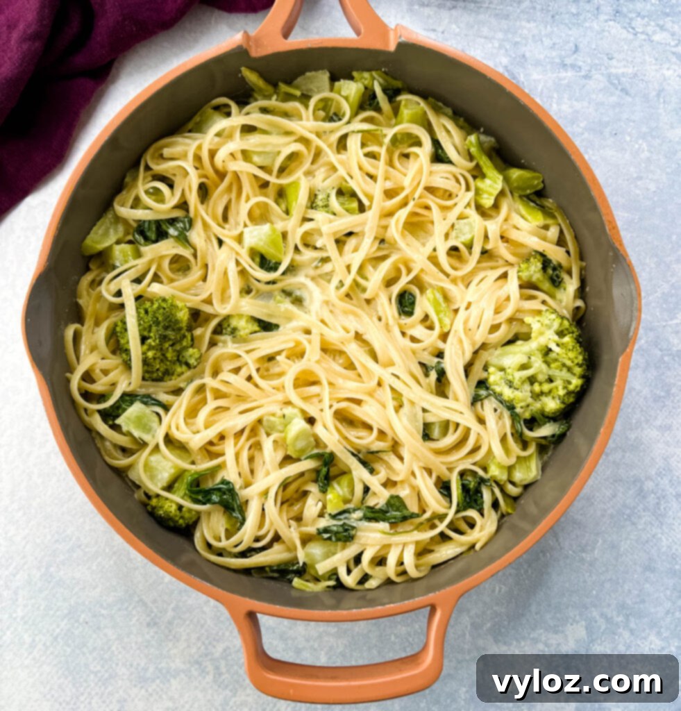 Creamy lemon pasta in a pan with fresh spinach and broccoli mixed in, steam rising.