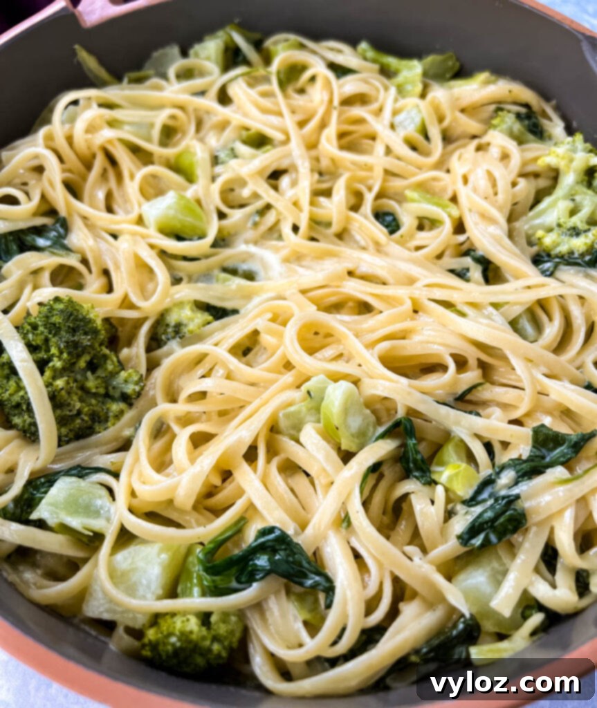 Lemon pasta with spinach and broccoli in a pan, garnished with fresh parsley.