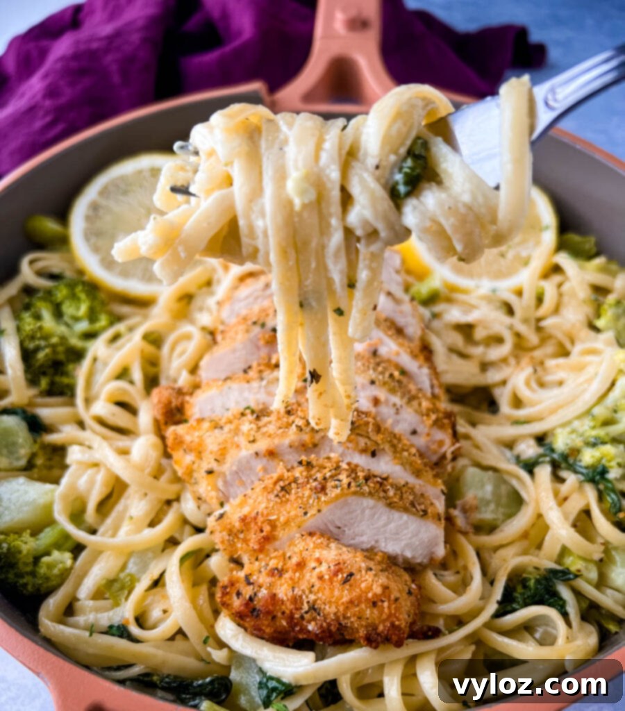 A fork twirled with creamy lemon pasta, showcasing the rich sauce and a piece of chicken.