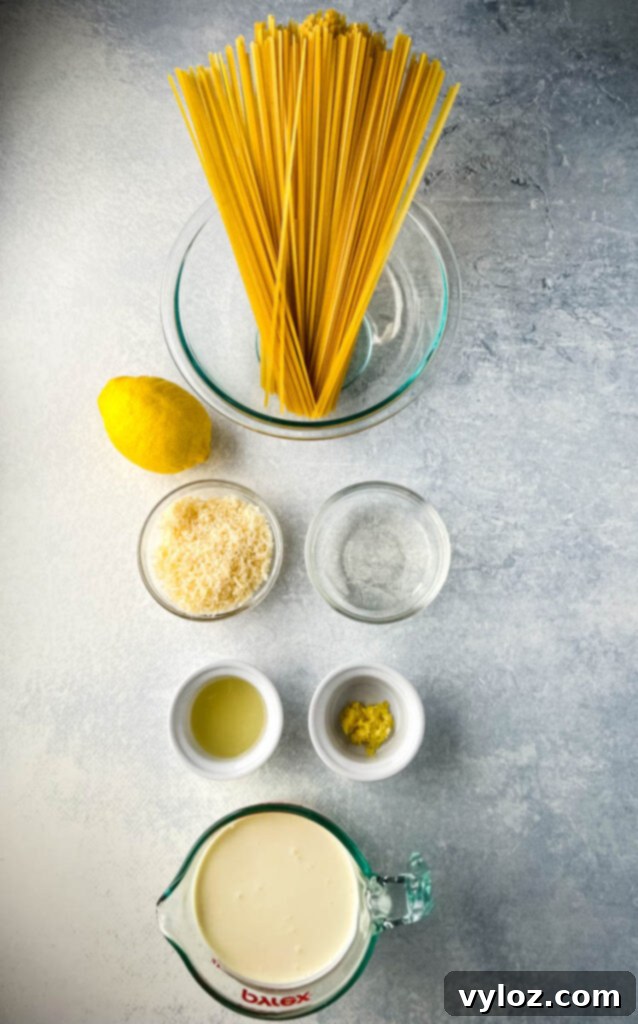 Ingredients for creamy lemon chicken pasta including fettuccine, fresh lemon, white wine, heavy cream, and Parmesan cheese in separate bowls.