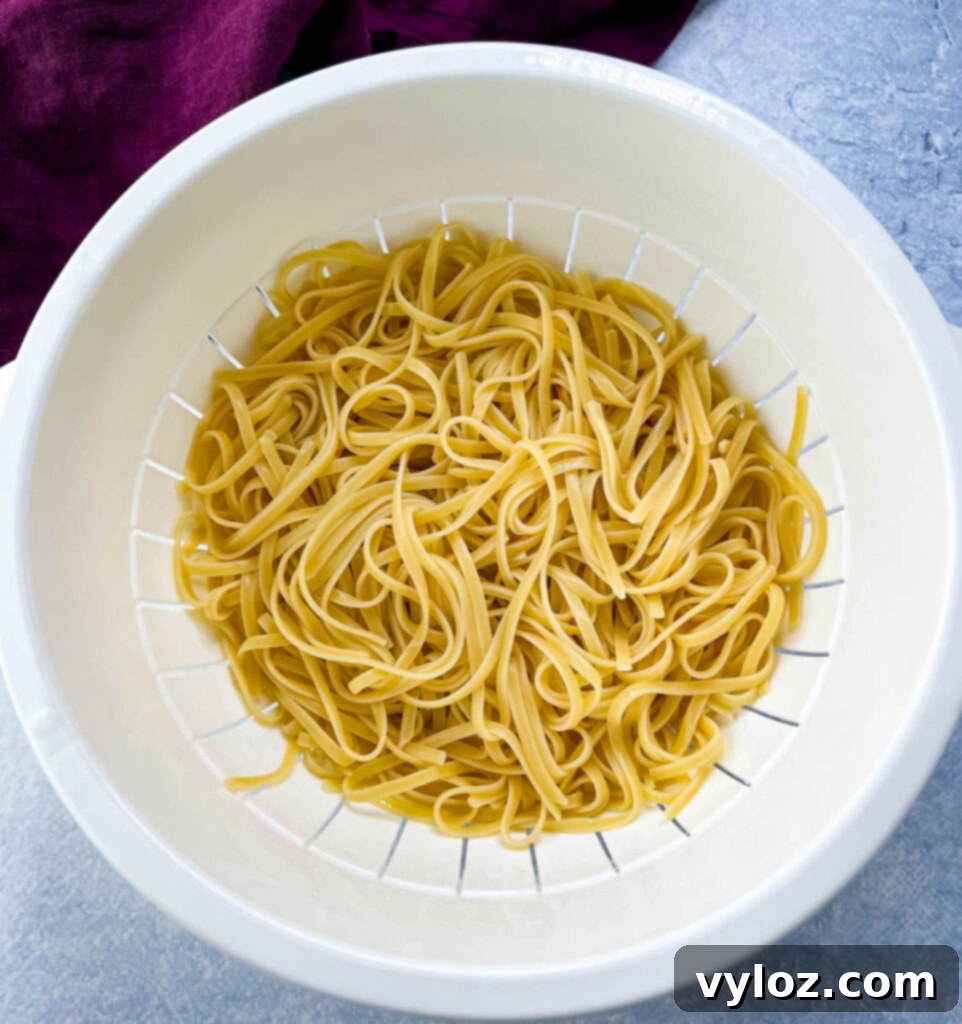 Cooked fettuccine pasta draining in a colander, steam rising.