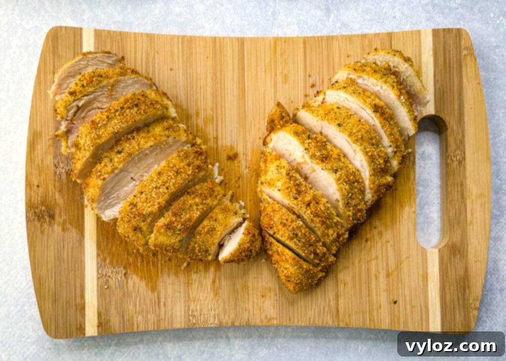 Sliced Parmesan breaded chicken resting on a wooden cutting board, showcasing its crispy crust and juicy interior.