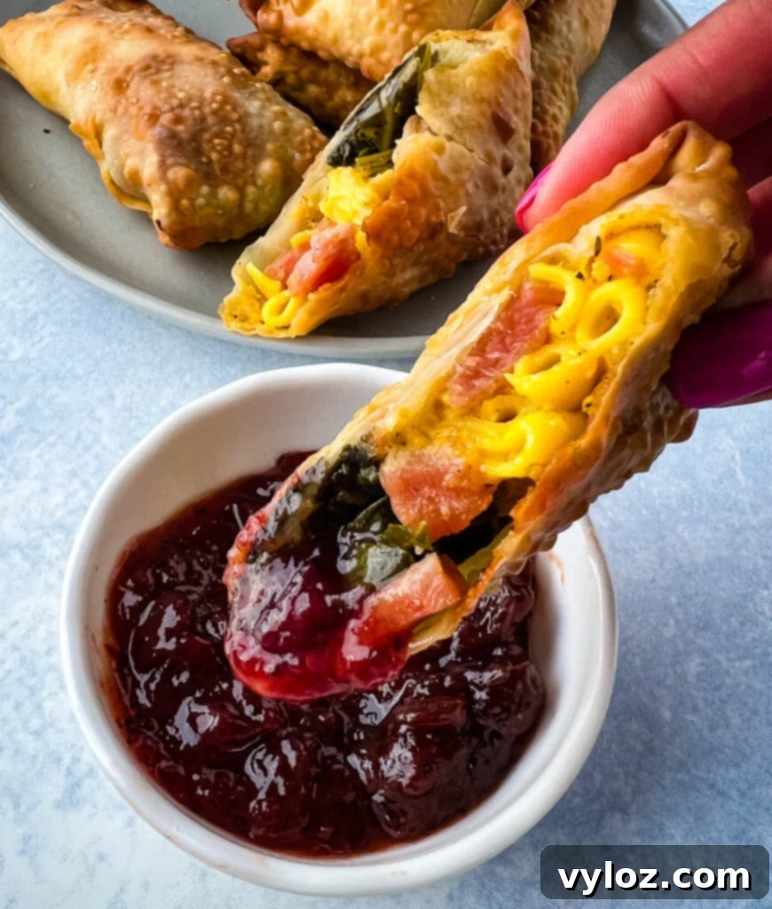 Person holding a golden-brown Thanksgiving soul food egg roll, dipping it into a vibrant cranberry sauce.