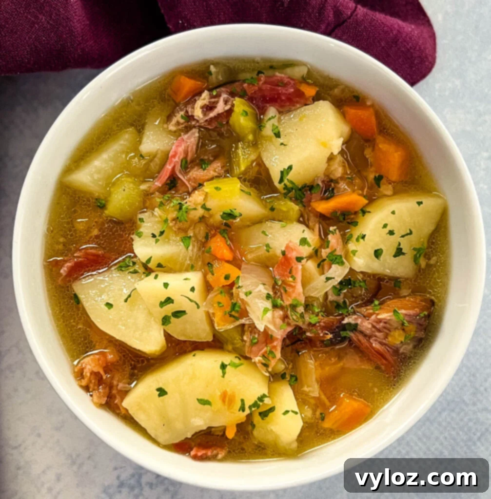 Hearty Slow Cooker Ham, Potato and Vegetable Soup 2 Hearty slow cooker ham and potato soup in a white bowl, garnished with fresh herbs.