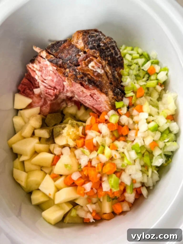 Hearty Slow Cooker Ham, Potato and Vegetable Soup 5 Uncooked slow cooker ham and potato soup ingredients, including diced vegetables and ham, arranged in a Crockpot before cooking.