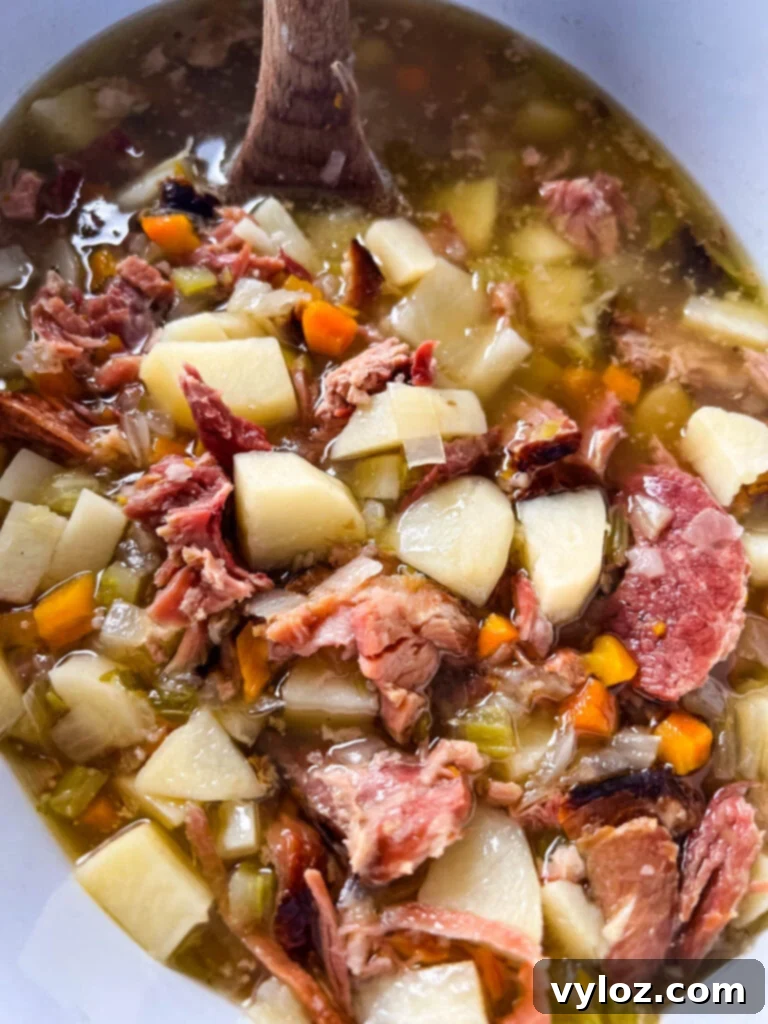 Hearty Slow Cooker Ham, Potato and Vegetable Soup 10 A cozy bowl of slow cooker ham and potato soup, garnished and steaming warmly.