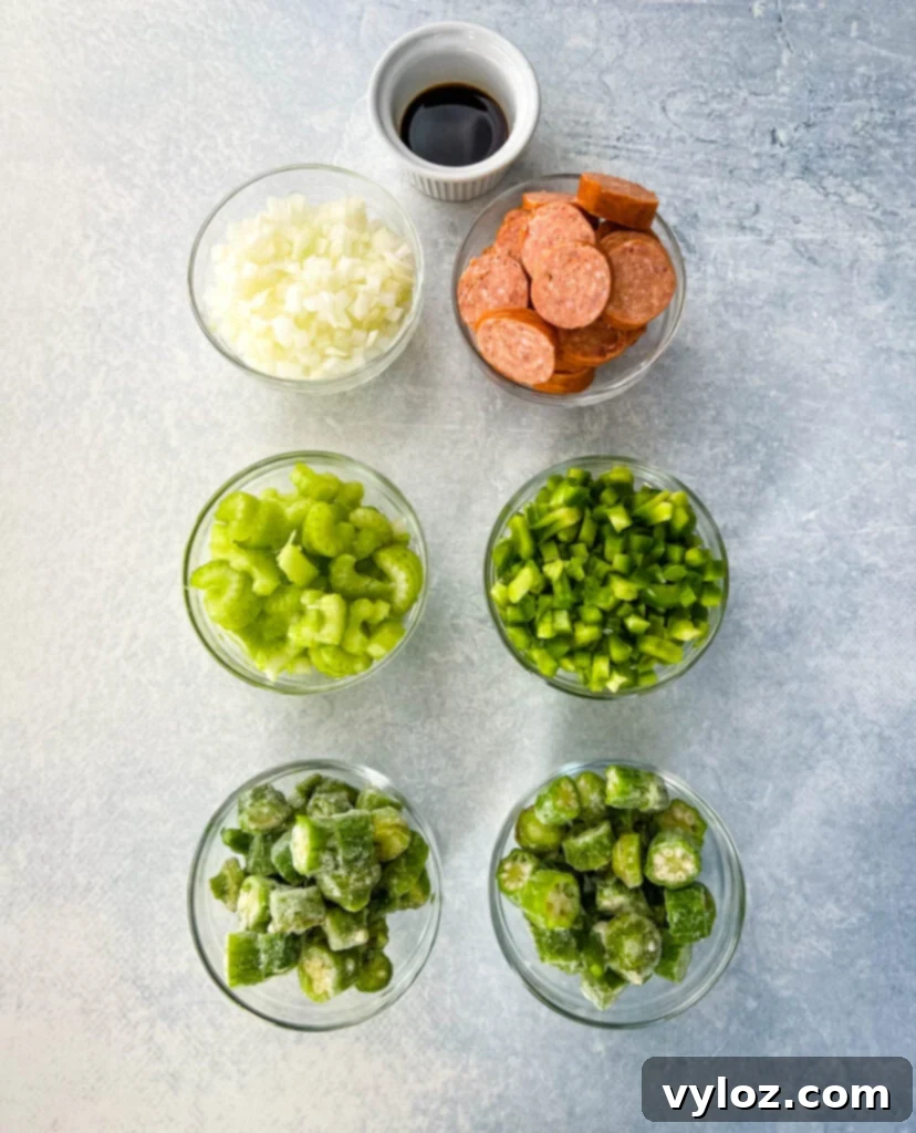 Bowls of prepped gumbo ingredients including chopped onions, green peppers, celery, sliced andouille sausage, okra, and Worcestershire sauce, demonstrating the classic 'Holy Trinity'.
