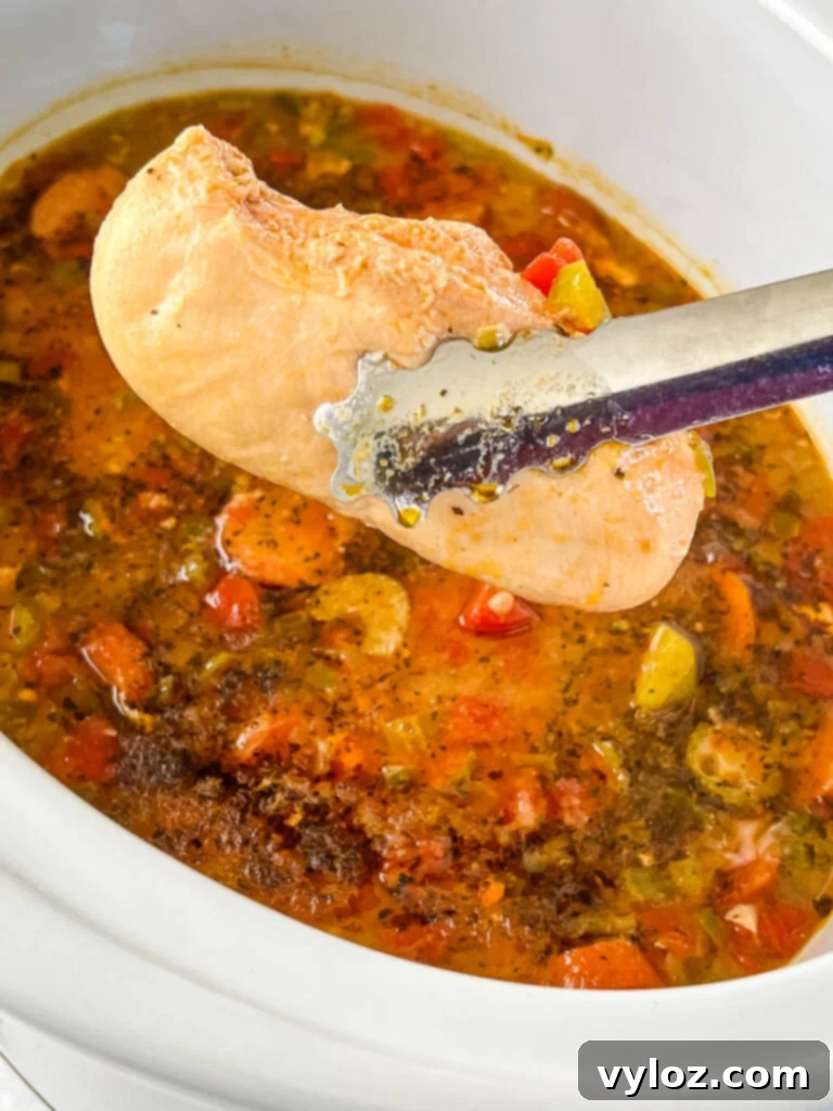 Cooked chicken breast being held by tongs, ready for shredding for the gumbo.