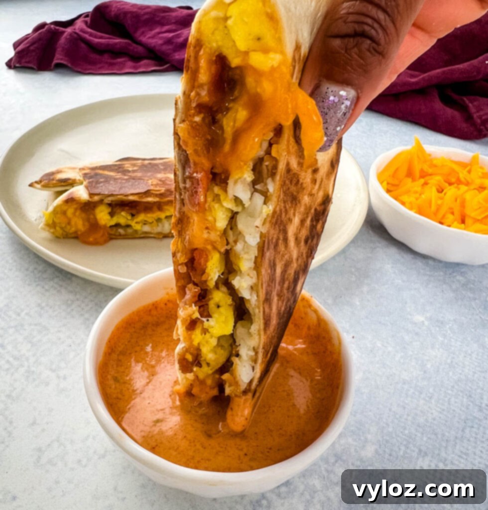 A breakfast crunchwrap being dipped into a bowl of creamy Taco Bell sauce, showcasing its delicious potential.