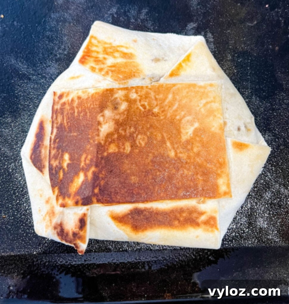 A breakfast crunchwrap cooking in a cast iron skillet, getting a perfect crispy crust.