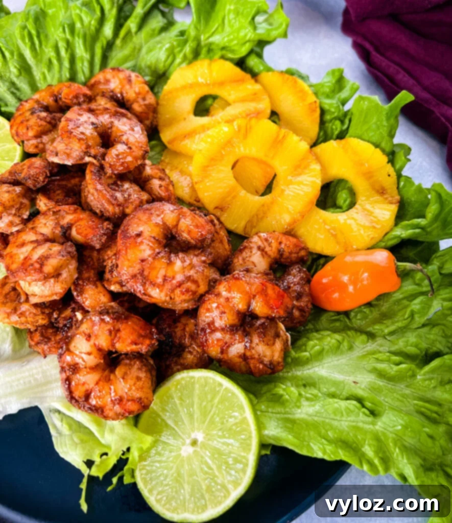 Delicious jerk shrimp served on a bed of fresh lettuce, garnished with pineapple chunks, lime wedges, and vibrant fresh peppers.