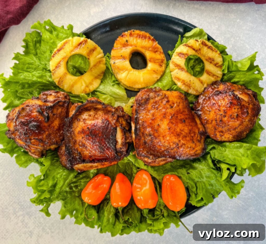 Bone-in Jamaican jerk chicken thighs on a plate with vibrant peppers and perfectly grilled pineapples, showcasing a complete meal.