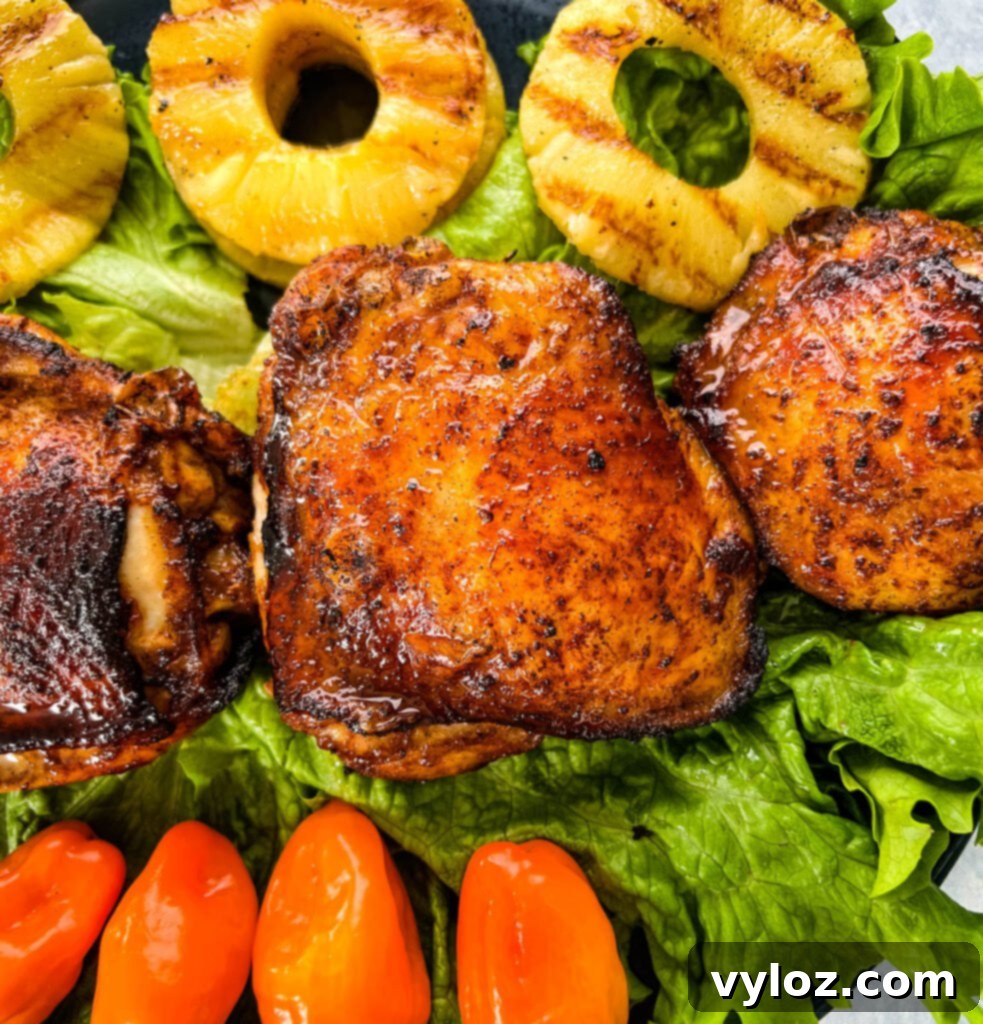 A close-up of succulent bone-in Jamaican jerk chicken thighs served alongside colorful bell peppers and caramelized grilled pineapple slices.