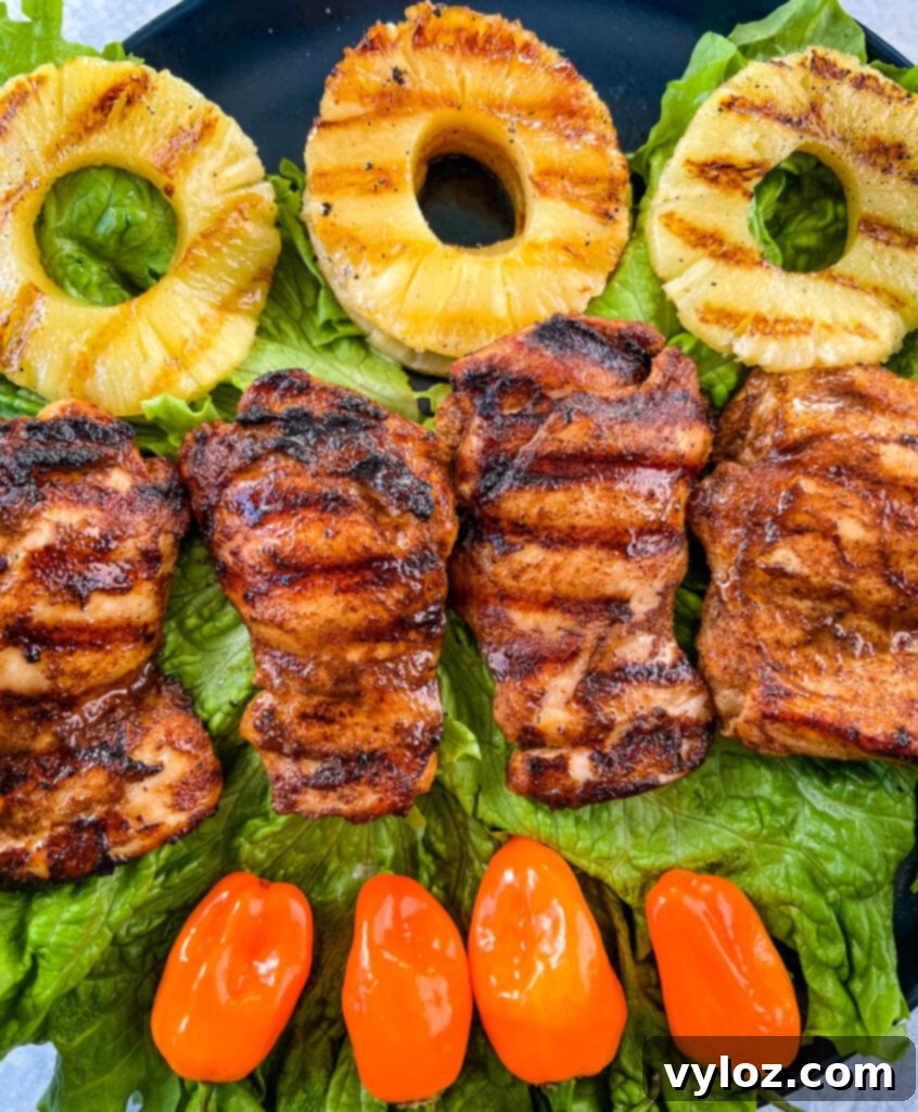 A vibrant plate of Jamaican jerk chicken thighs, artfully arranged with grilled peppers and sweet pineapple.