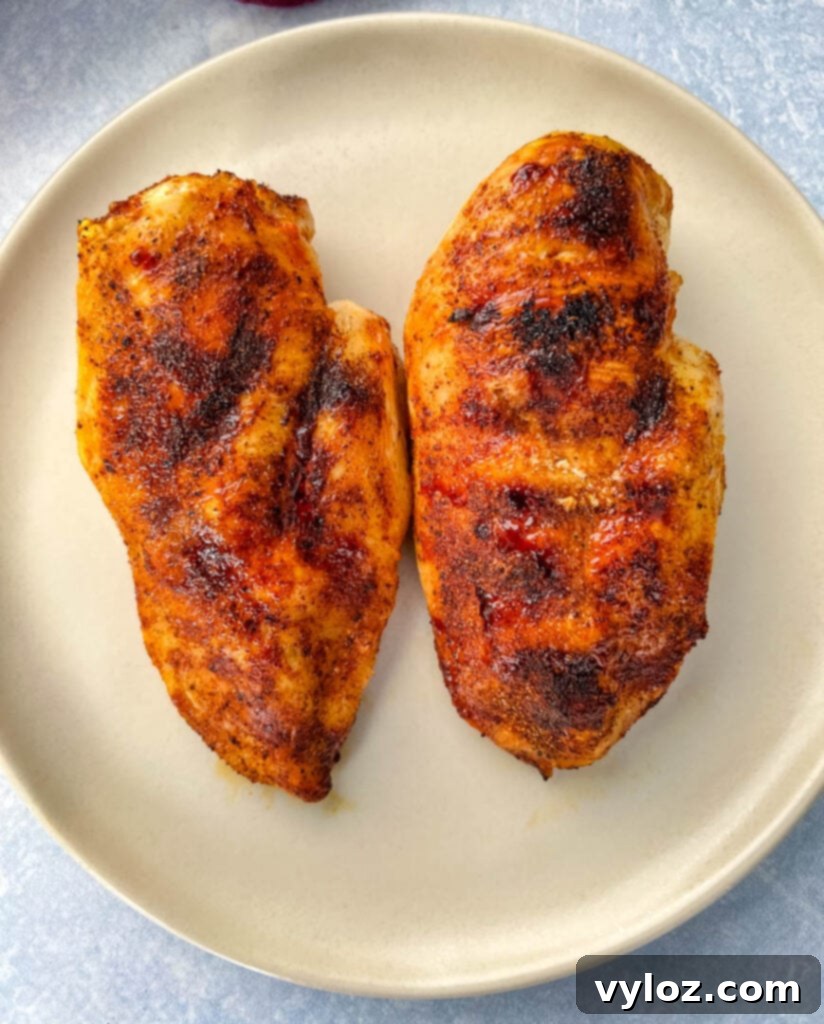 Two cooked chicken breasts on a white plate, garnished with fresh herbs