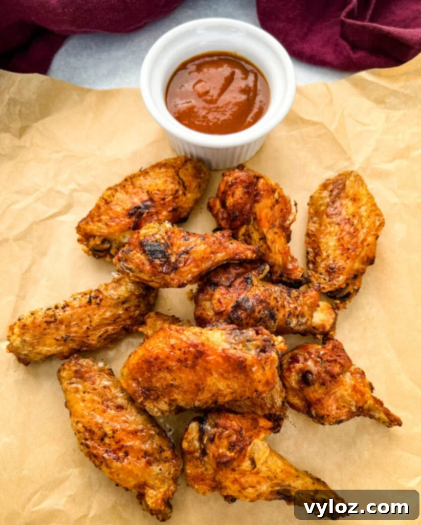 Cooked chicken wings on brown paper, drizzled with BBQ sauce, showcasing their crispy texture.