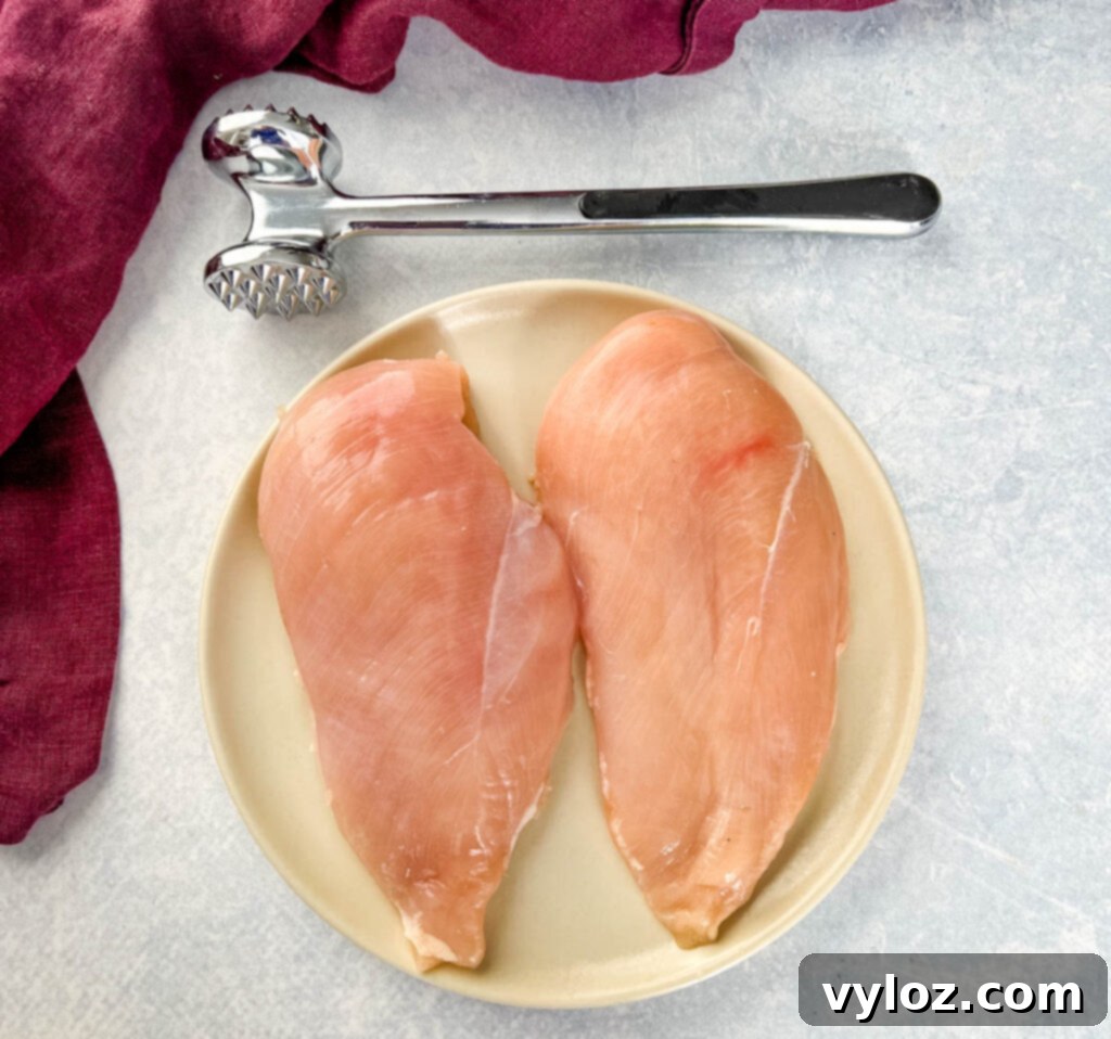 raw chicken breasts on a plate with a mallet