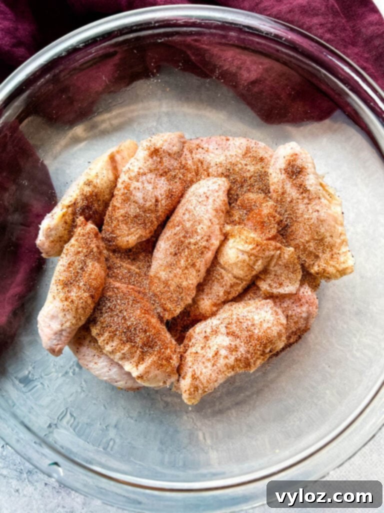 Raw chicken wings being tossed with dry rub spices and flour in a glass bowl, ready for coating.