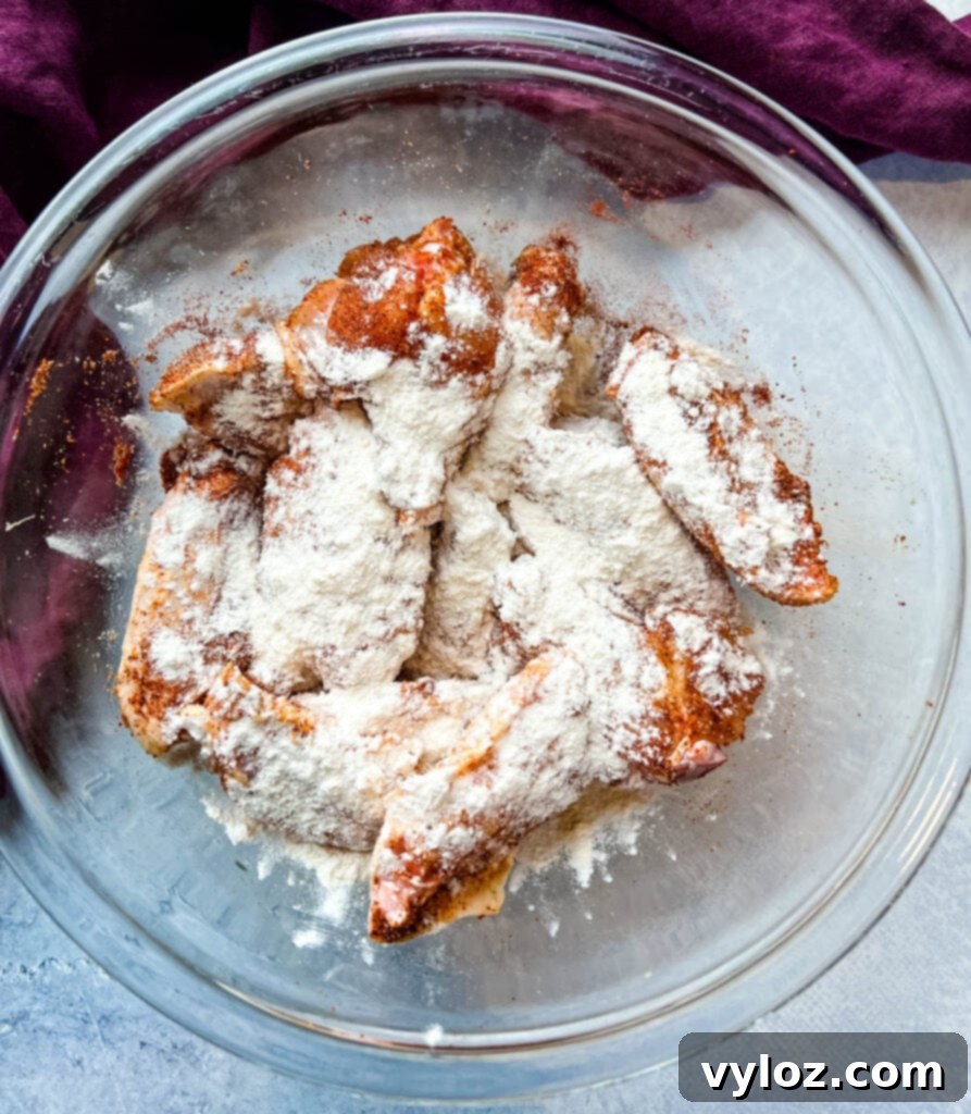 A close-up view of raw chicken wings generously coated in dry rub and flour, showcasing the even application.