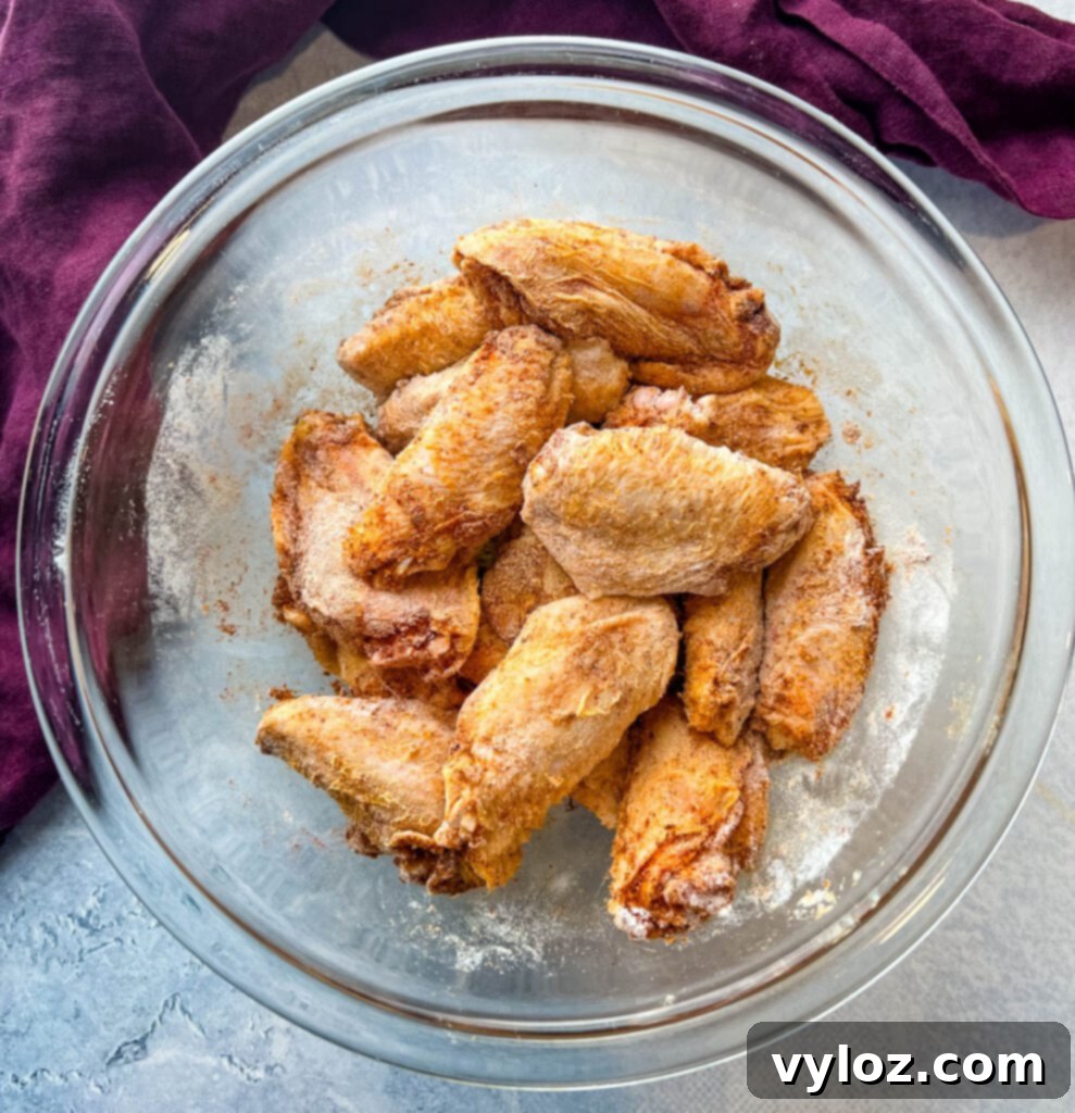 Another perspective of perfectly coated raw chicken wings in a glass bowl, illustrating readiness for cooking.