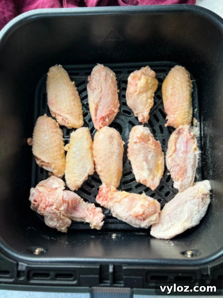 Raw chicken wings coated with dry rub arranged in an air fryer basket, ready for cooking.