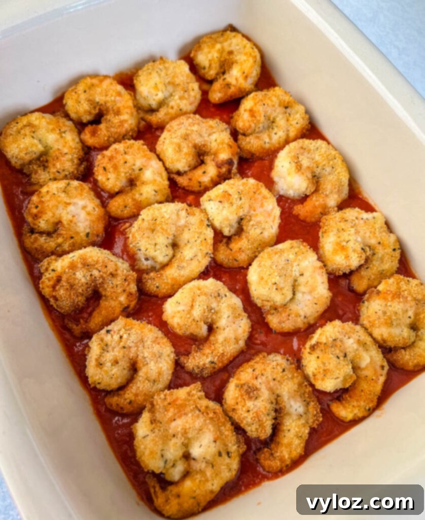 A close-up of fully prepared Shrimp Parmesan in a baking dish, glistening with sauce and cheese.