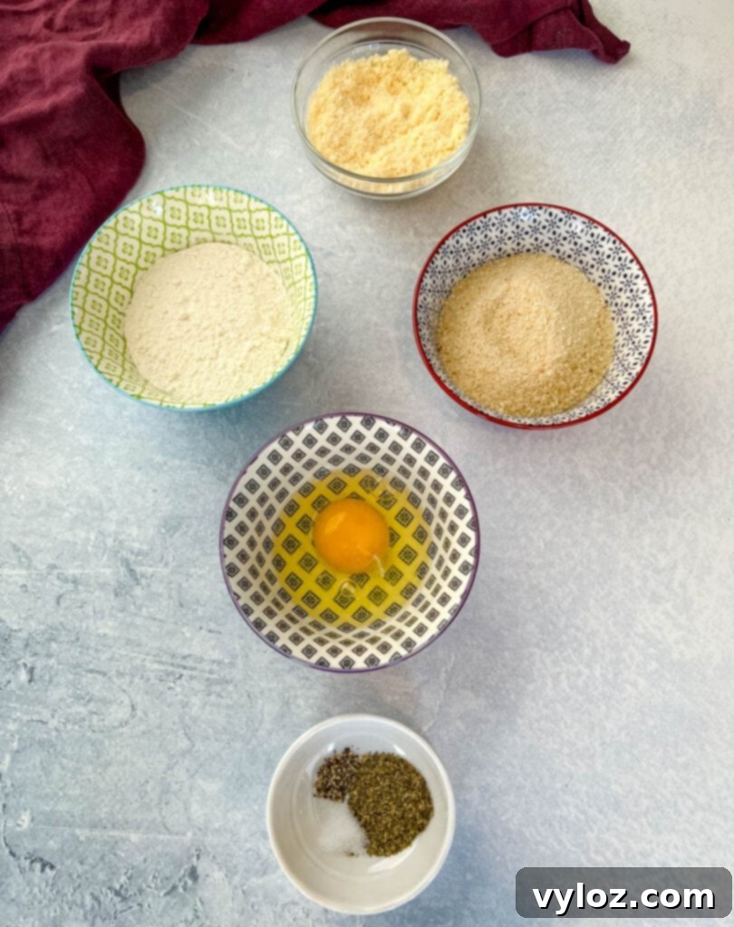 A display of breading ingredients: breadcrumbs, flour, egg, spices, and Parmesan cheese in separate bowls.