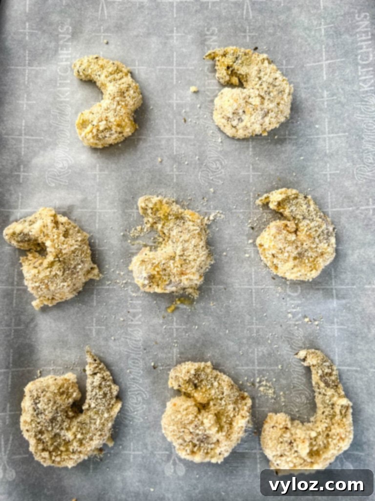 Crispy breaded shrimp arranged on a baking sheet, ready for the oven.