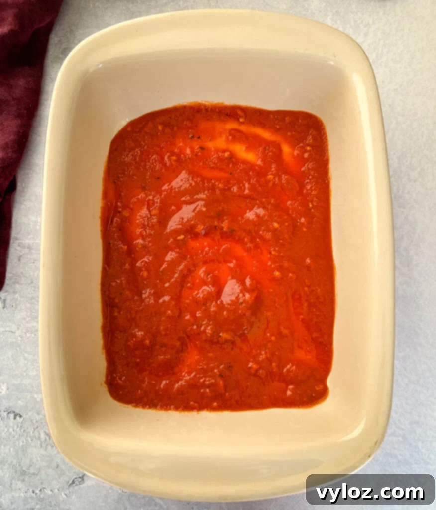 Vibrant marinara sauce spread evenly at the bottom of a baking dish.