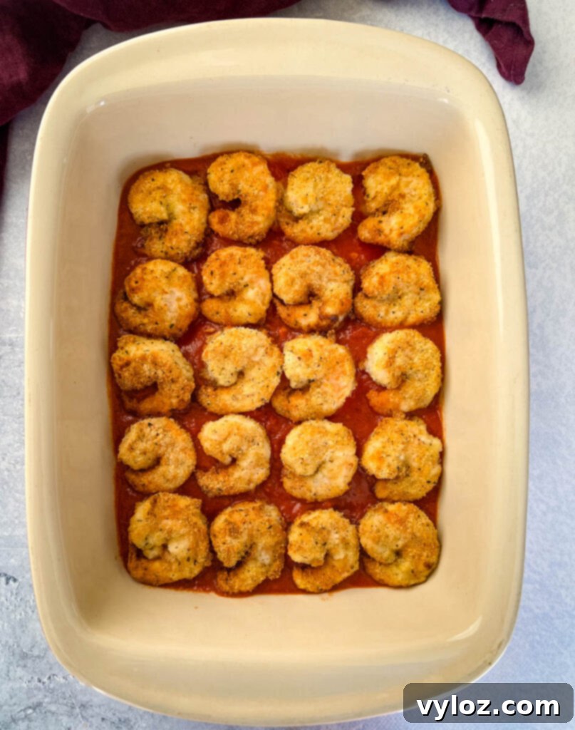 Shrimp Parmesan arranged over marinara sauce in a baking dish before final cheese topping.