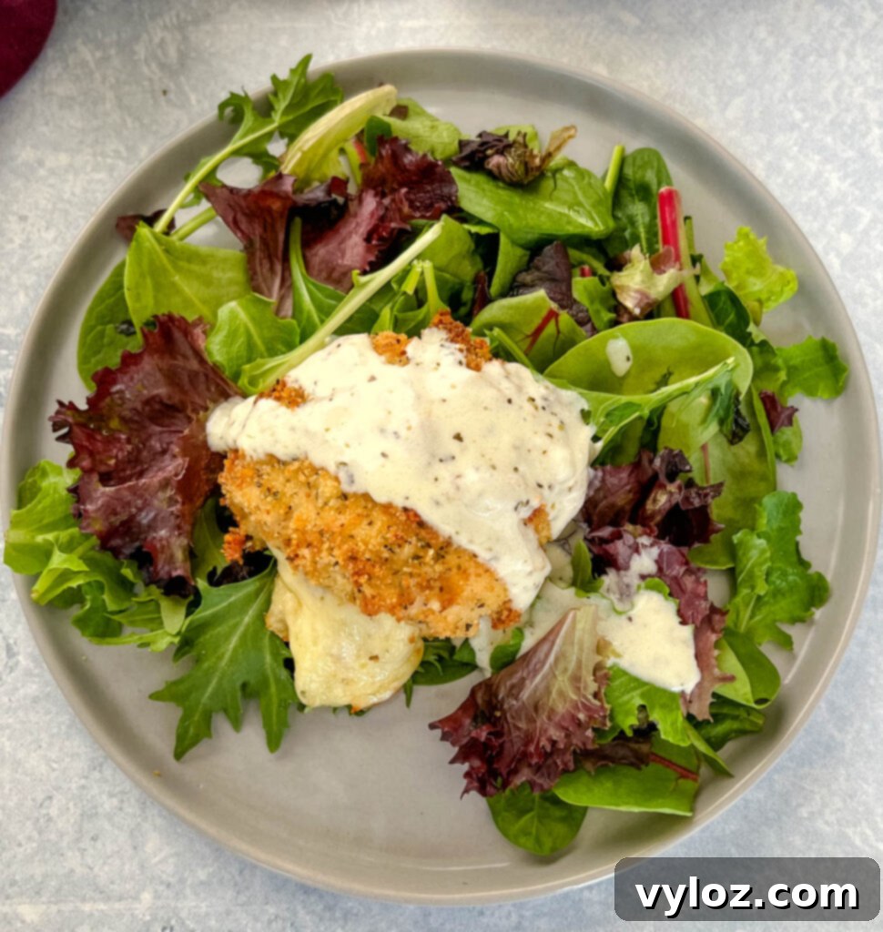 mozzarella stuffed chicken breast on a plate with salad and drizzled in cream sauce