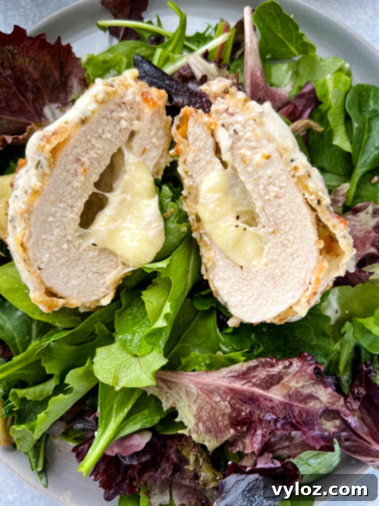 mozzarella stuffed chicken breast on a plate with salad and drizzled in cream sauce