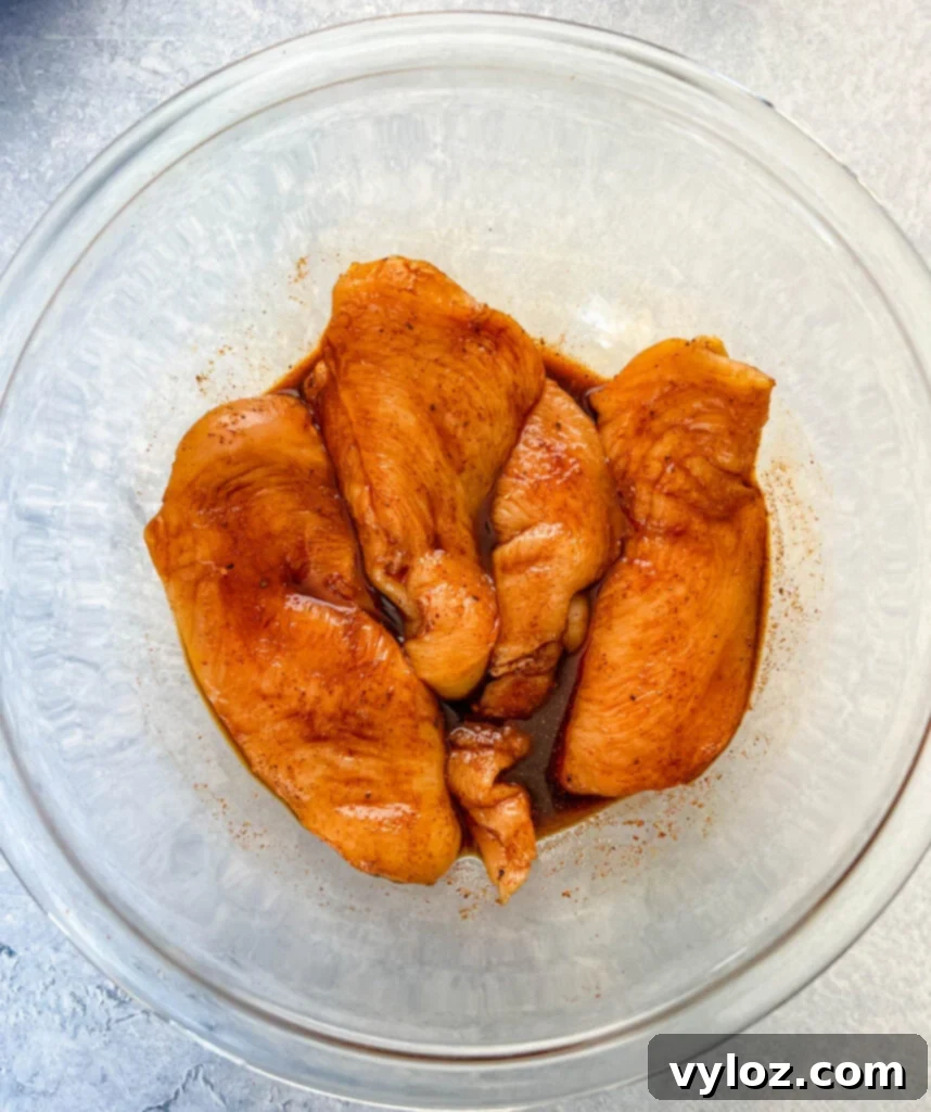 Raw chicken breasts in a glass bowl, coated in soy sauce and dry rub, ready for smoking.