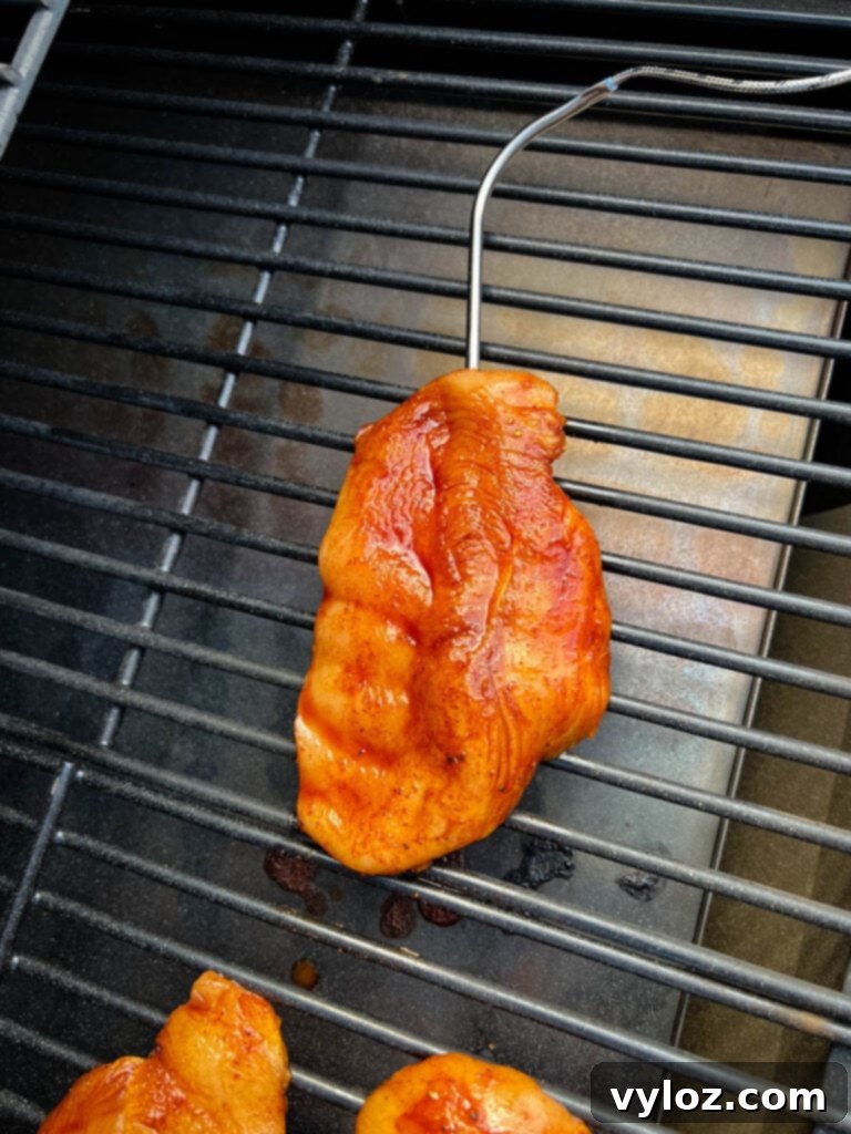 Raw chicken breasts on a Traeger smoker grill with a meat probe inserted, monitoring temperature.