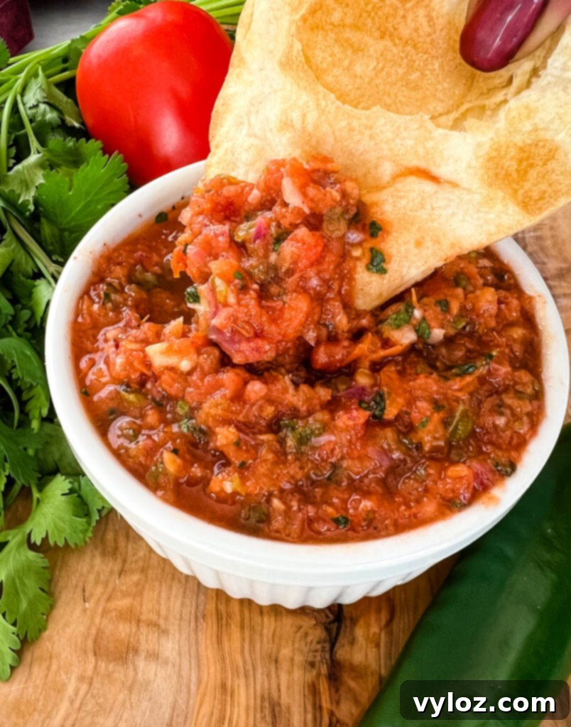 Smoky Salsa Secrets 11 A hand holding a tortilla chip generously loaded with homemade smoked salsa, ready to be enjoyed.