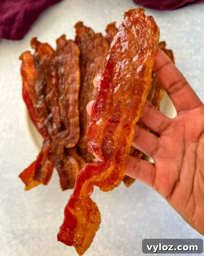 Ultimate Traeger Smoked Bacon 12 person holding a piece of smoked bacon