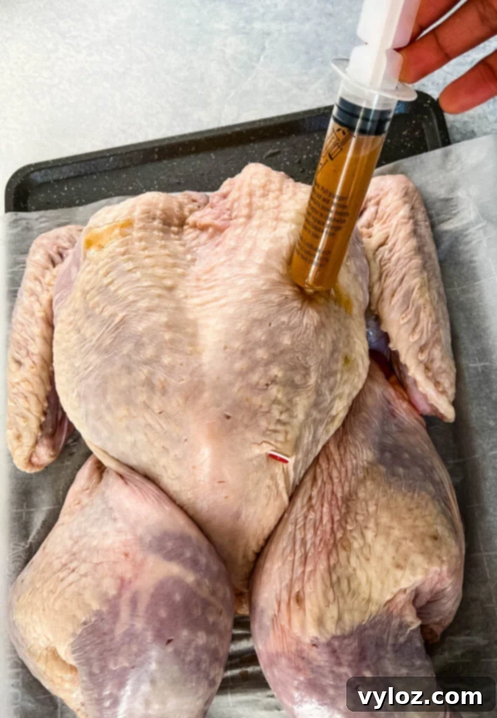 Smoked Spatchcock Turkey on the Traeger 7 A close-up shot of a person injecting marinade into raw turkey breast.