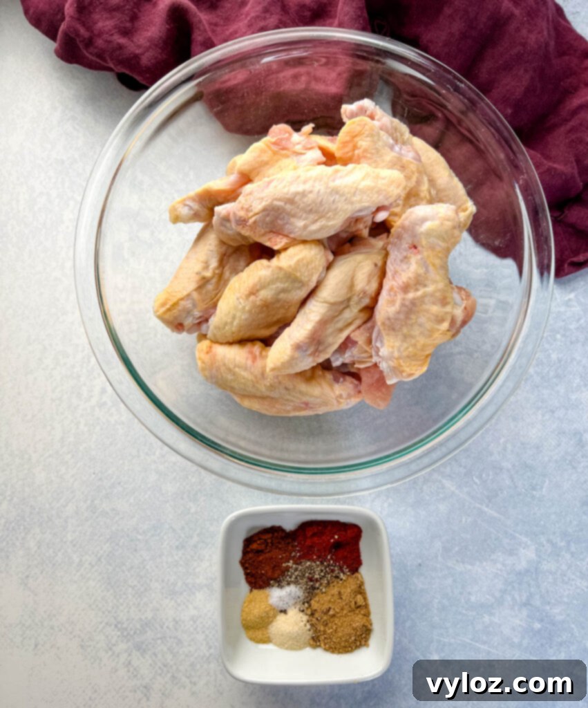 Raw chicken wings in a glass bowl alongside a smaller bowl of dry rub spices