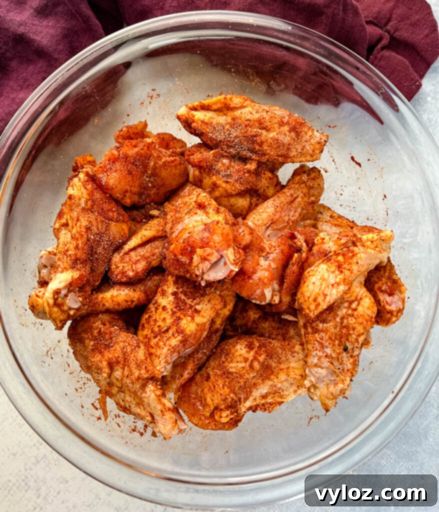 Raw chicken wings in a glass bowl coated in a rich, dark dry rub