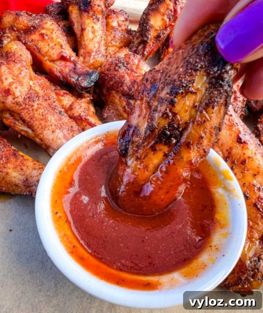 A person holding a Traeger smoked chicken wing, freshly dipped in BBQ sauce, showcasing its delicious appeal