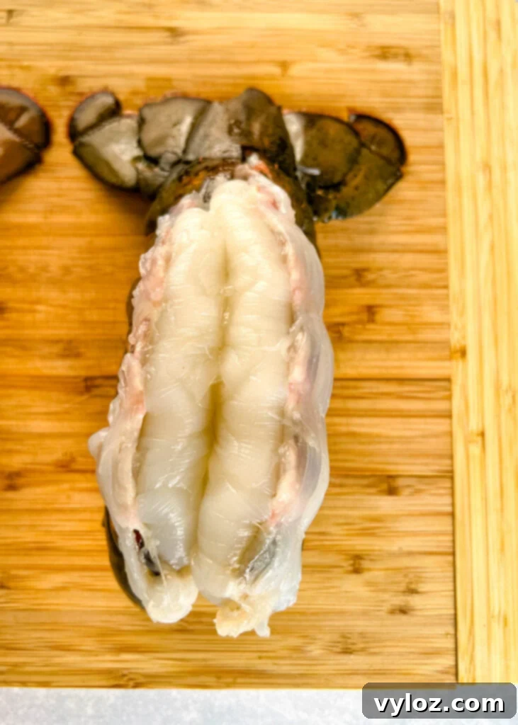 Effortless Smoked Lobster Tails 7 A raw, butterflied lobster tail with the meat delicately propped over the shell on a cutting board, ready for seasoning.