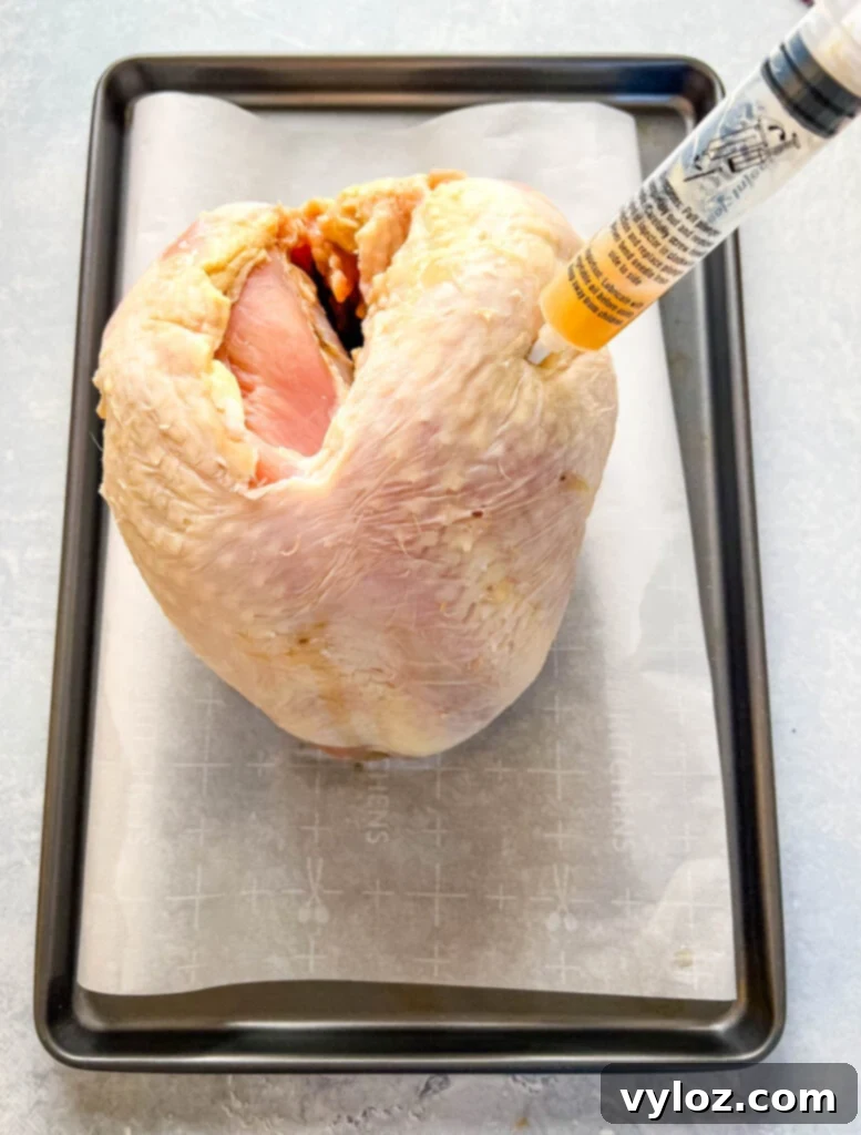 Juicy Traeger Smoked Turkey Breast 6 Raw turkey breast on parchment paper after being injected with a flavorful butter marinade, ready for smoking.