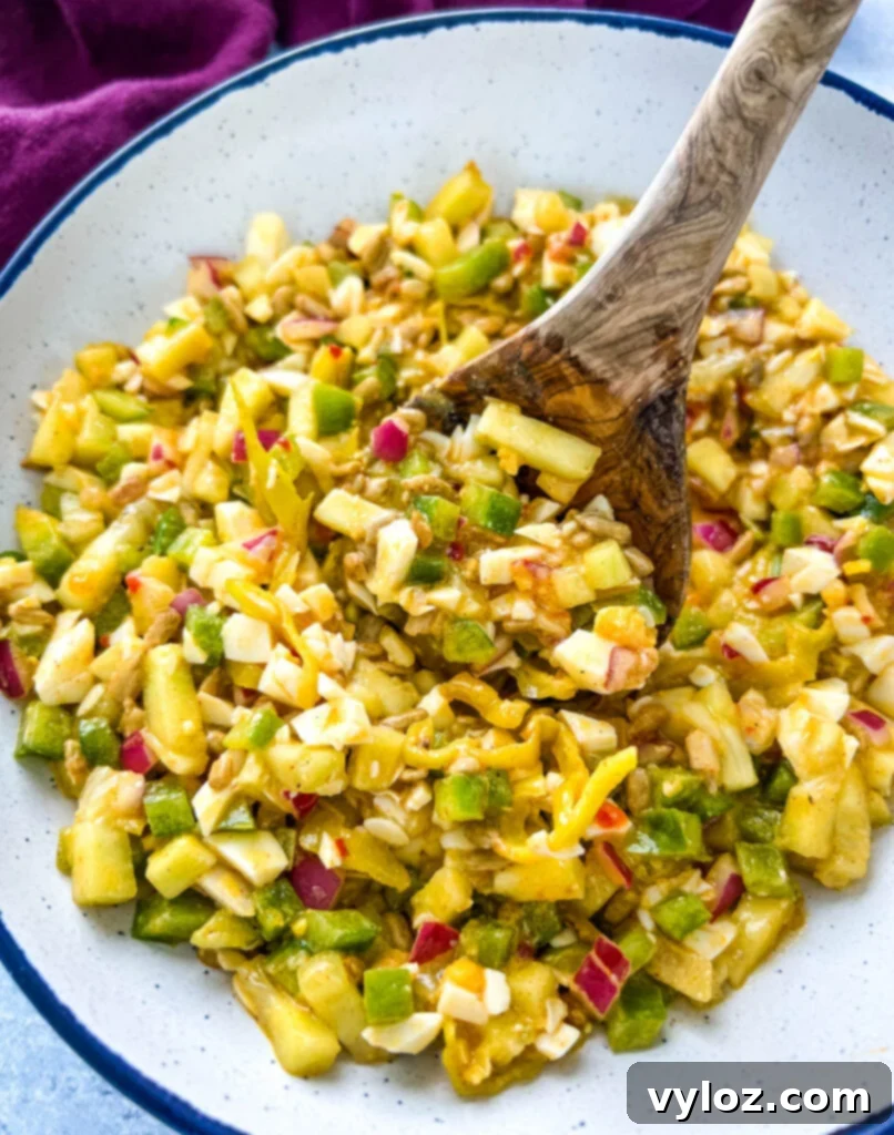 Your Go-To Hot Girl Summer Salad 2 Hot Girl Summer Salad, a vibrant mix of vegetables, eggs, and sunflower seeds, served in a white bowl with a wooden spoon.