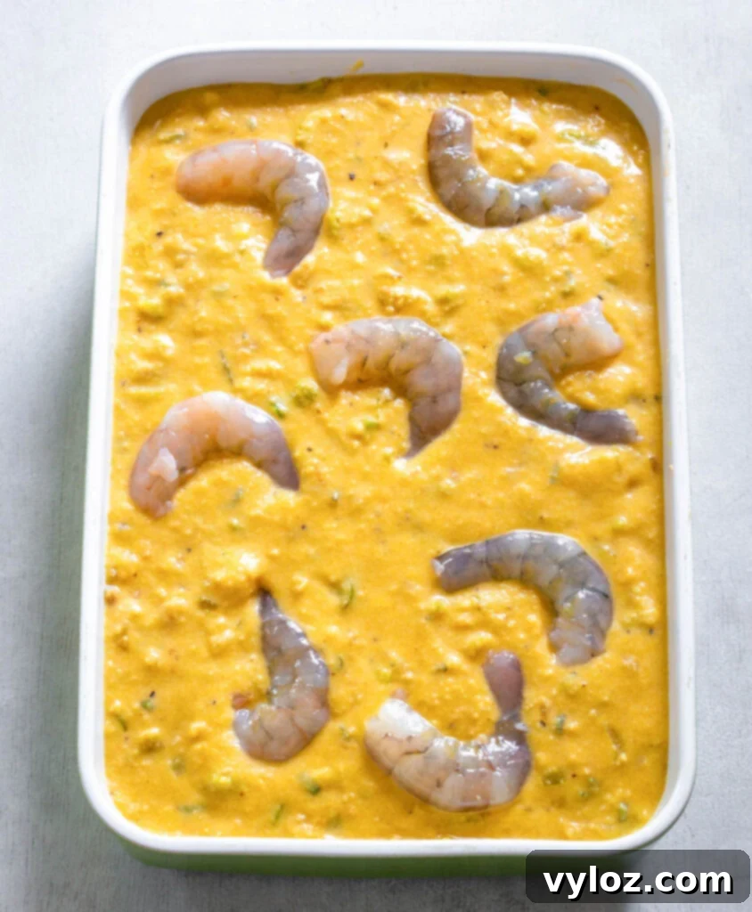 The Ultimate Seafood Dressing 8 Unbaked seafood cornbread dressing with visible shrimp arranged in a baking dish, ready for the oven.