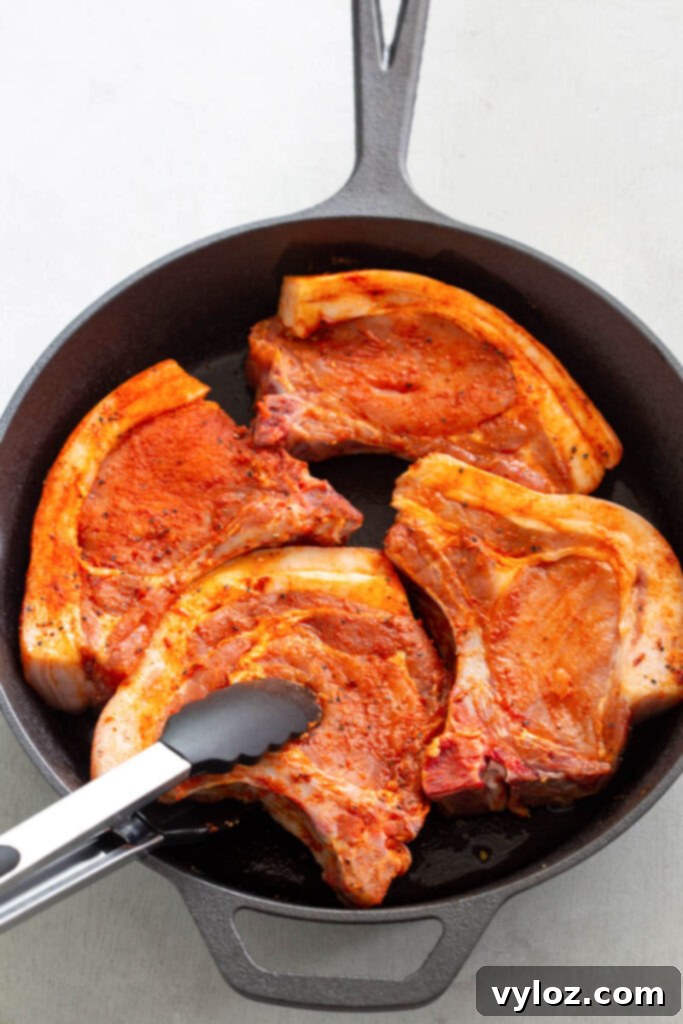 Soulful Southern Smothered Pork Chops 5 raw seasoned bone in pork chops in a cast iron skillet