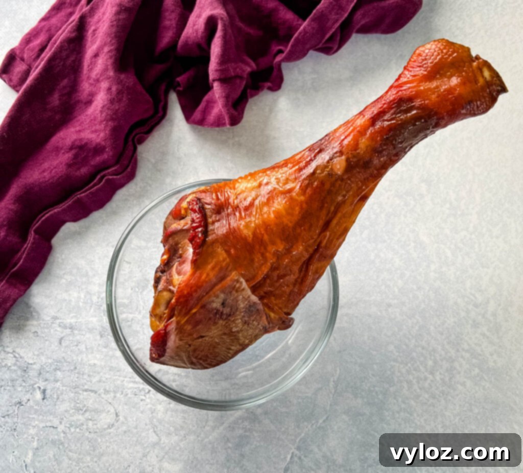 A glistening smoked turkey leg rests in a glass bowl, ready to infuse a pot of Southern butter beans with rich flavor.