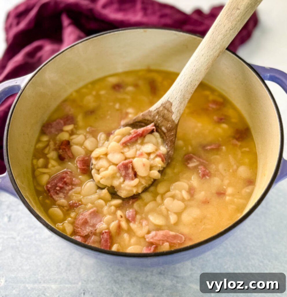 A spoonful of Southern butter lima beans, perfectly creamy and flavorful, being served from a Dutch oven.